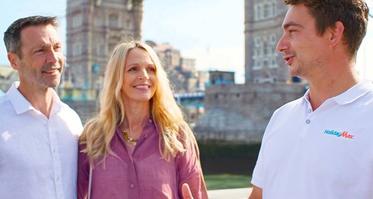 Tour guide in HolidayMax shirt converses with couple along the Thames with Tower Bridge behind.