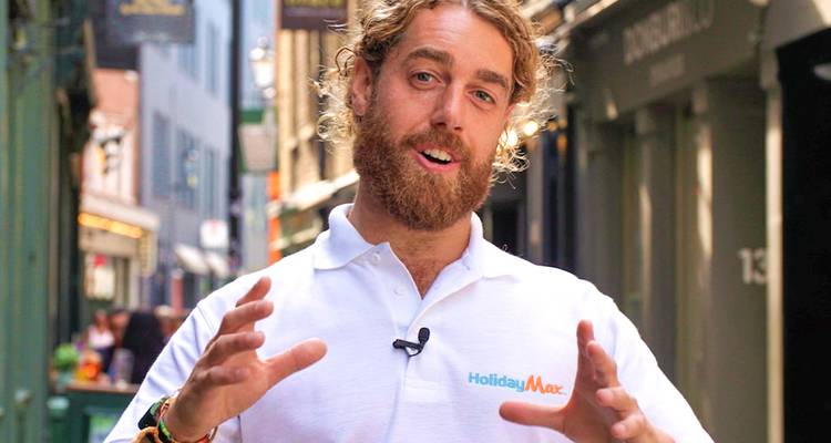 Bearded HolidayMax tour leader gesturing energetically in a narrow European alleyway.