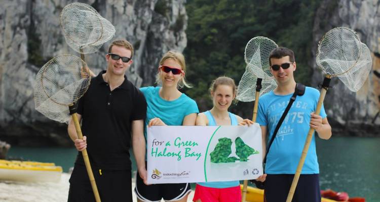 Gruppe von Freiwilligen, die ein Banner und Müllnetze halten, mit Karstfelsen und Kajaks im Hintergrund