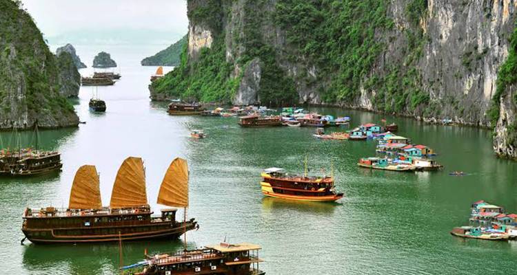 Les jonques traditionnelles en bois aux voiles beiges et les maisons flottantes du village ancré dans une baie étroite d'un vert émeraude