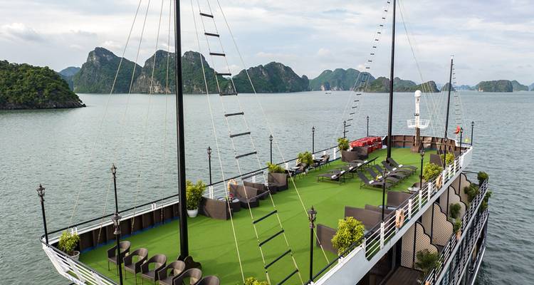 Pont supérieur d'un navire de croisière avec pelouse artificielle verte, chaises longues et îles karstiques environnantes