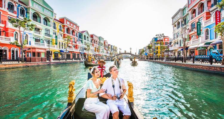 Romantic couple seated in a gondola while a gondolier rows down a pastel-colored canal street
