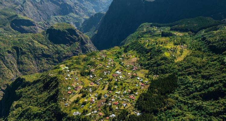 Drone view of a lush village nestled within dramatic cirque walls on Réunion Island.