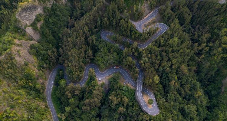 Serpentine mountain road winds through dense forest seen from above.