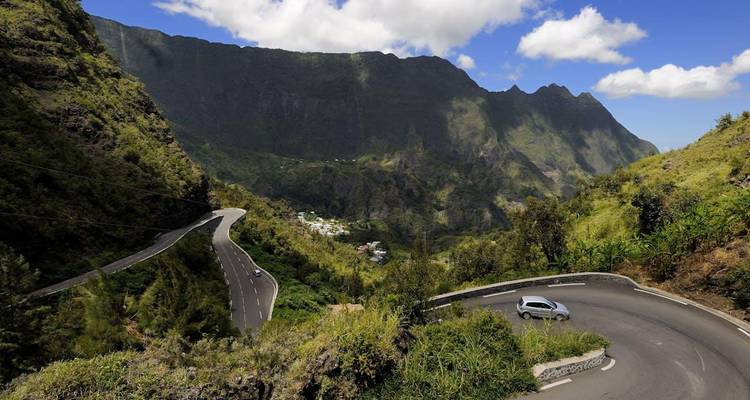 Hairpin turn carved into green mountains with a single car navigating the bend.