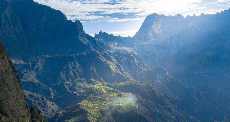 Sunlit mist drifts over a vast serrated valley system on Réunion Island.
