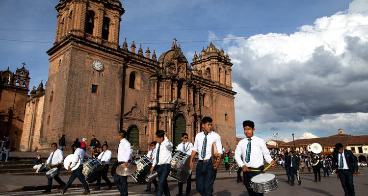 La fanfare scolaire défile au son des tambours devant la façade en pierre d'une église historique de Cusco sous un ciel dynamique