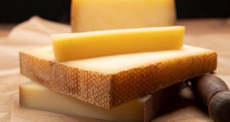 Gros plan de fromage suisse tranché sur du papier parchemin avec un couteau à manche en bois.