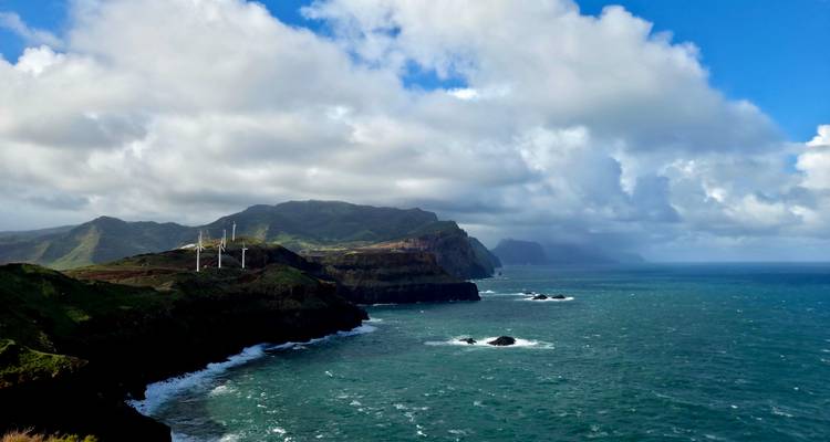 Les éoliennes se dressent sur des falaises côtières spectaculaires avec des mers turquoise et des collines ondulantes sous des nuages cumulonimbus.