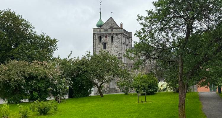 Tour de pierre médiévale partiellement cachée par des arbres fruitiers à l'intérieur d'un parc verdoyant par une journée grise.