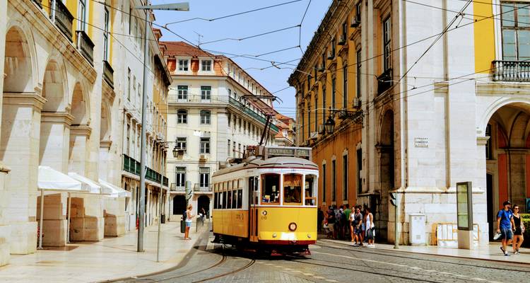 Ikonische gele tram die door smalle, zonnige straten van Lissabons historische Baixa-wijk draait.