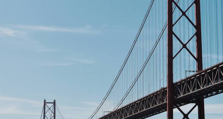 Minimalistische compositie van de kabels en torens van de 25 de Abril-hangbrug tegen een heldere blauwe lucht.