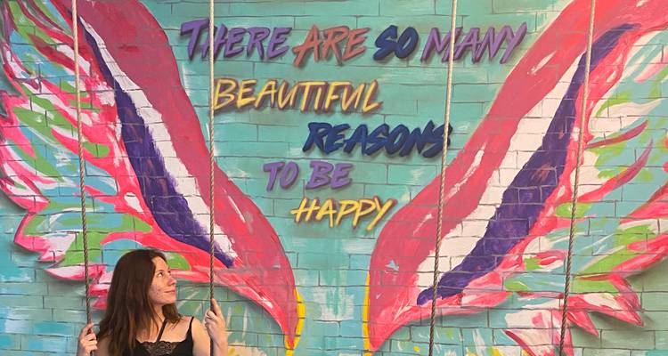 Colorful wings mural with motivational quote and a woman posing on a swing in front.