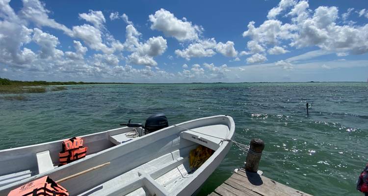 Small white motorboat tied to a wooden jetty on bright turquoise water under a blue sky with scattered clouds