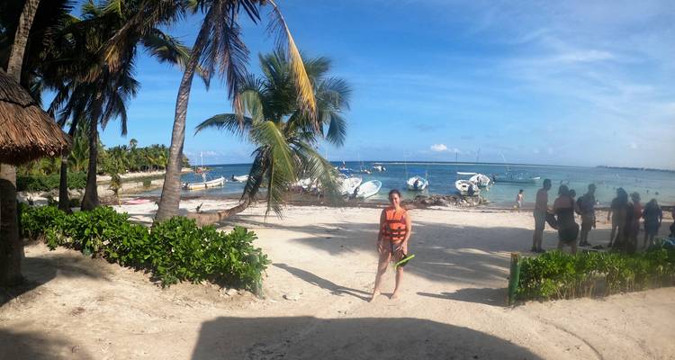 Tropical beach scene with palm trees, moored boats and tourists preparing to snorkel