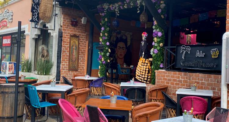 Colorful open-air Mexican restaurant decorated with flowers, brick arches and a Frida Kahlo mural