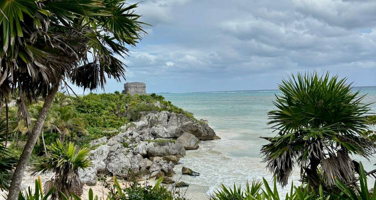 Iconic cliff-top Mayan ruin overlooking turquoise Caribbean waters framed by palm trees