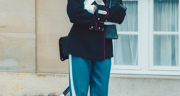 Garde royal en uniforme officiel tenant un fusil se tenant près d'un bâtiment en pierre pâle