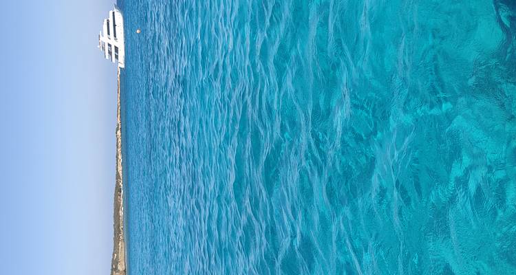 Wide expanse of vibrant turquoise water with a distant white yacht and barren shoreline.