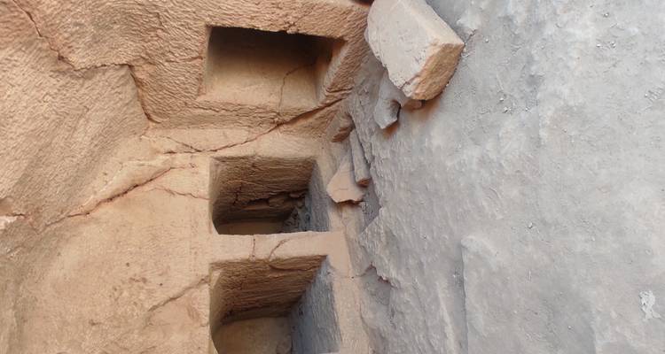 Interior of an ancient tomb with rectangular niches carved into rough stone walls.