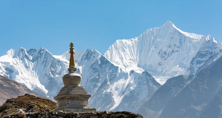 A small Buddhist stupa stands on a grassy ridge with gleaming snowy summits forming a majestic backdrop.