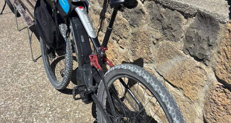 Gros plan de la roue arrière du vélo électrique et du cadre appuyés contre un mur de pierre brute