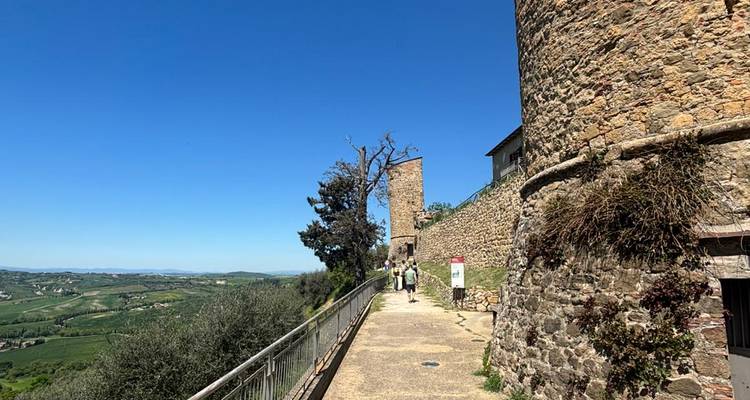 Allée pavée de pierre le long de tours médiévales surplombant une vallée verdoyante avec des touristes devant