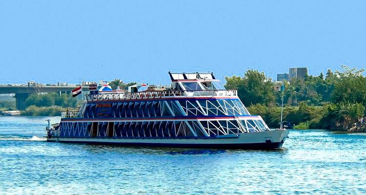 Un colorido crucero de varios pisos navega por un amplio y tranquilo río rodeado de árboles verdes bajo un cielo azul despejado.