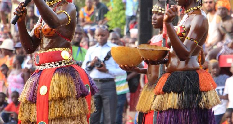 Traditional dancers in colorful layered skirts perform before a large crowd at an outdoor festival.