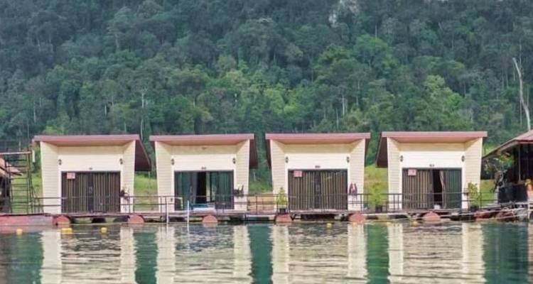Rangée de petites cabines flottantes compactes reflétées dans les eaux calmes d'un lac avec une forêt dense à l'arrière-plan.