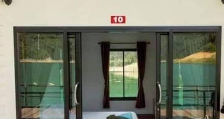 Les portes vitrées d'un bungalow flottant s'ouvrent vers un lac émeraude calme entouré de collines couvertes de jungle.