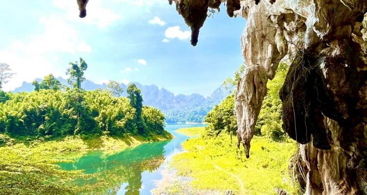 Vue depuis l'intérieur d'une grotte calcaire donnant sur une rivière turquoise sinueuse, une jungle luxuriante et des pics karstiques lointains sous un ciel dégagé.