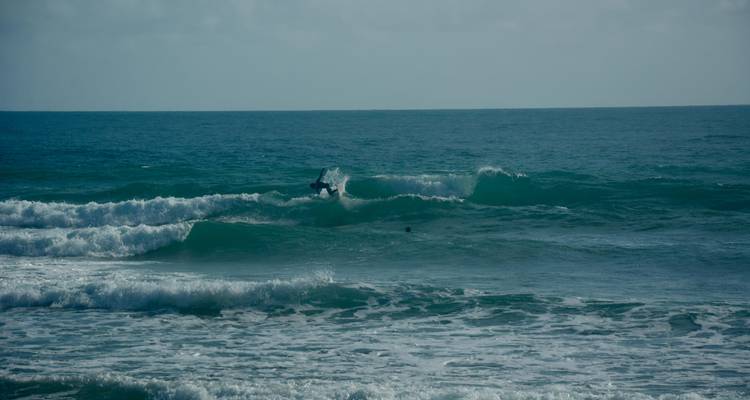 Un surfeur effectuant une manoeuvre de carving sur une vague bleu-vert foncé avec de l'écume blanche illuminée par une lumière tardive
