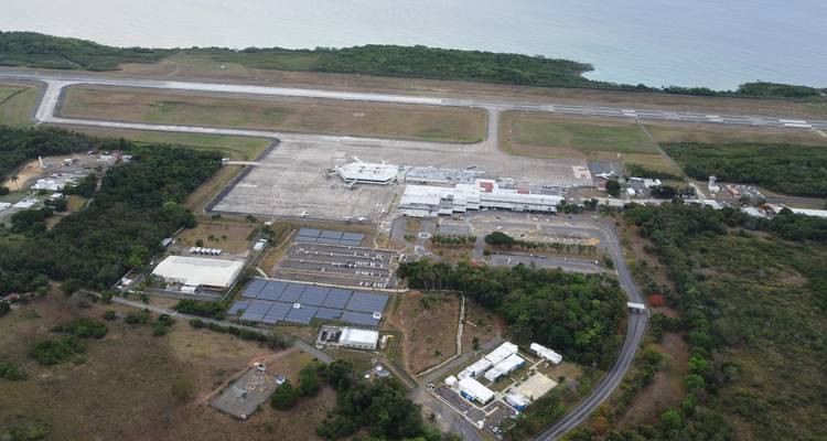 Vue aérienne d'un aéroport côtier avec pistes d'atterrissage, bâtiments terminaux et forêt environnante