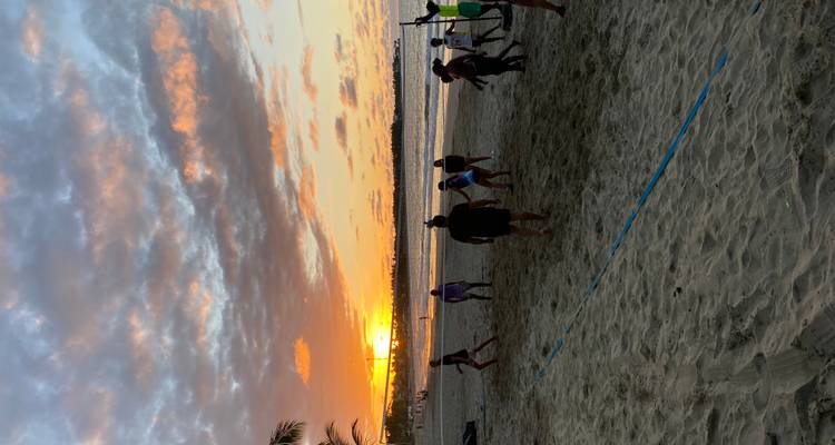 Groupe de personnes jouant au volley-ball de plage au coucher du soleil avec un ciel orange dramatique