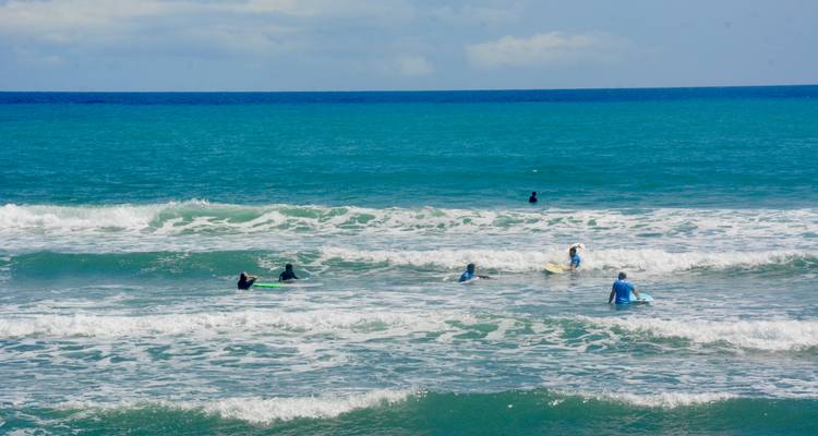 Des surfeurs allongés sur leurs planches attendant les vagues dans une eau turquoise cristalline sous un ciel dégagé.