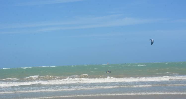 Kitesurfeur lointain sur une mer verte agitée sous un vaste ciel bleu, composition minimaliste.