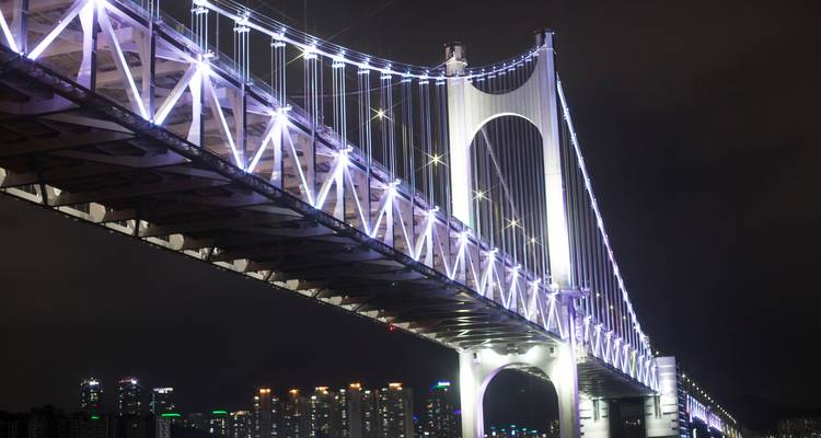 Beleuchtete Gwangan Diamond Bridge in Busan, die sich nachts über die Lichter der Stadt erstreckt.