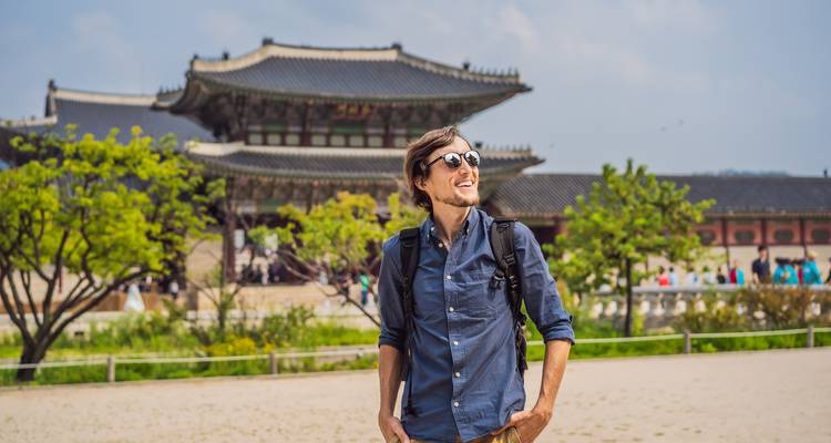 Lächelnder Reisender mit Rucksack vor einem traditionellen Palastpavillon in Seoul.