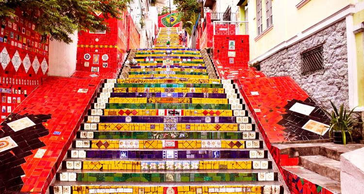Escaleras Escadaria Selarón cubiertas de mosaicos vibrantes ascendiendo entre los coloridos edificios de Río de Janeiro.
