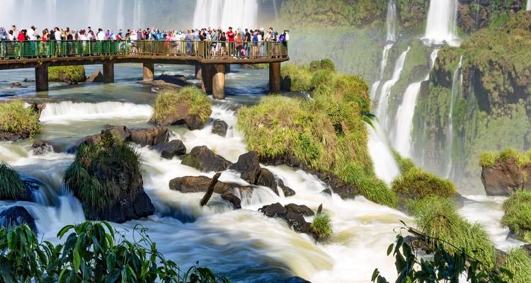 Pasarela abarrotada sobre las Cataratas del Iguazú con cascadas poderosas y exuberante vegetación por todos lados.