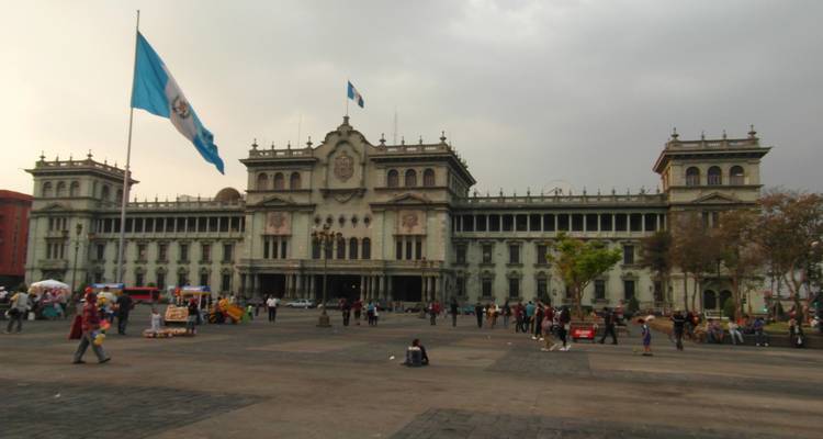 Las multitudes se reúnen en la plaza principal frente al Palacio Nacional de la Ciudad de Guatemala bajo cielos grises.