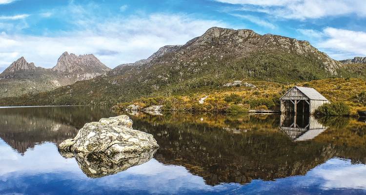 Lac aux eaux cristallines reflétant des montagnes escarpées et un hangar à bateaux rustique sous un ciel bleu éclatant