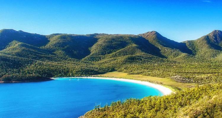 Panoramic view of a curved white-sand beach bordered by turquoise sea and forested mountains