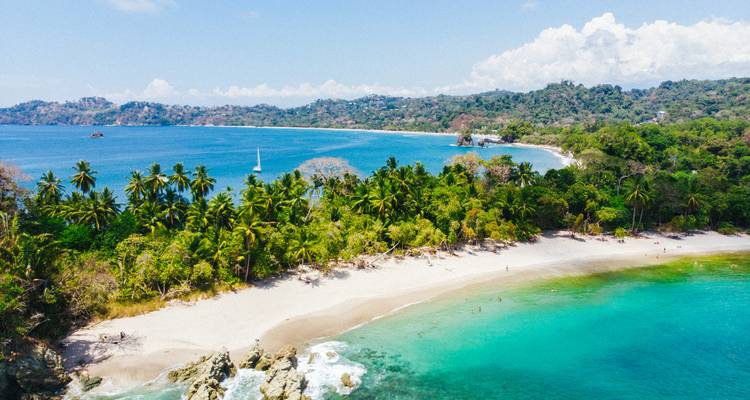 Vue aérienne d'une plage tropicale en forme de croissant et d'une péninsule verdoyante entourées d'eau turquoise.