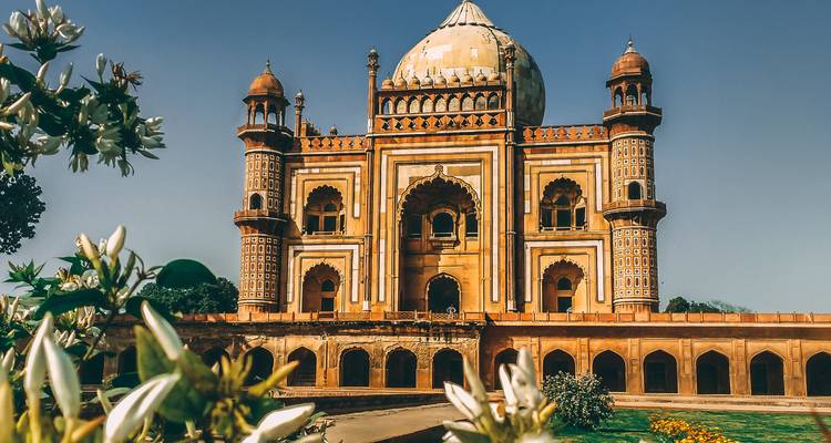 Elegantes Safdarjung-Mausoleum aus der Mogul-Ära, eingerahmt von blühenden weißen Blüten unter klarem Himmel.