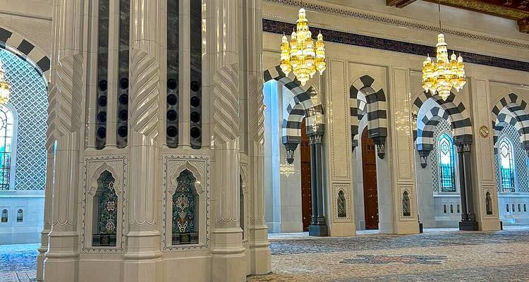 Interior lujoso de una mezquita omaní con pilares de mármol rayado y candelabros ornamentados.