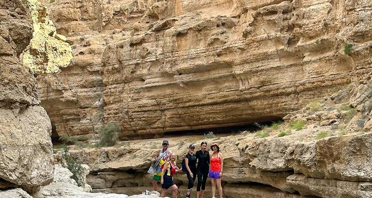 Pequeño grupo de senderistas posando en un cañón de wadi rocoso rodeado de paredes de piedra en capas.