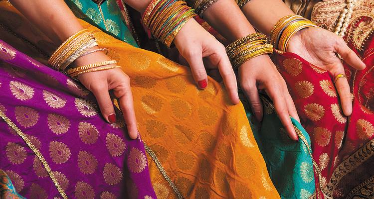 Gros plan des mains de femmes ornées de bracelets reposant sur des saris aux motifs éclatants.