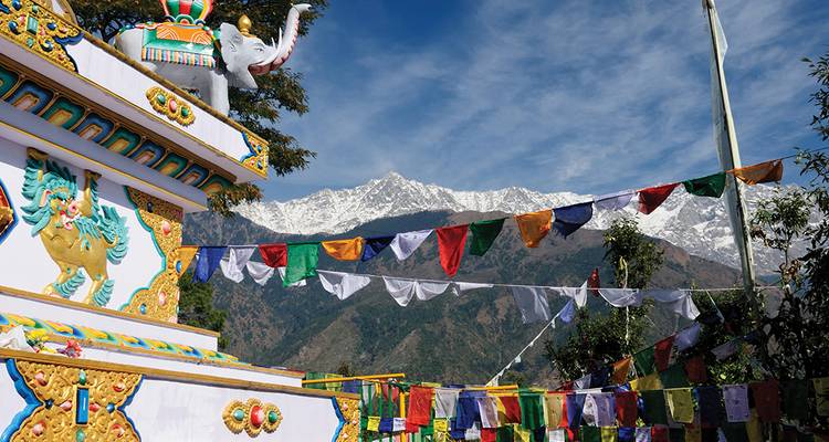 Des drapeaux de prière colorés flottent à côté d'un stupa aux vives couleurs avec les pics enneigés de l'Himalaya en arrière-plan.